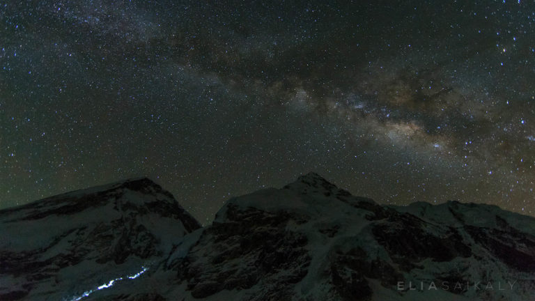 The milky way rises above above two mountain peaks with many stars at night