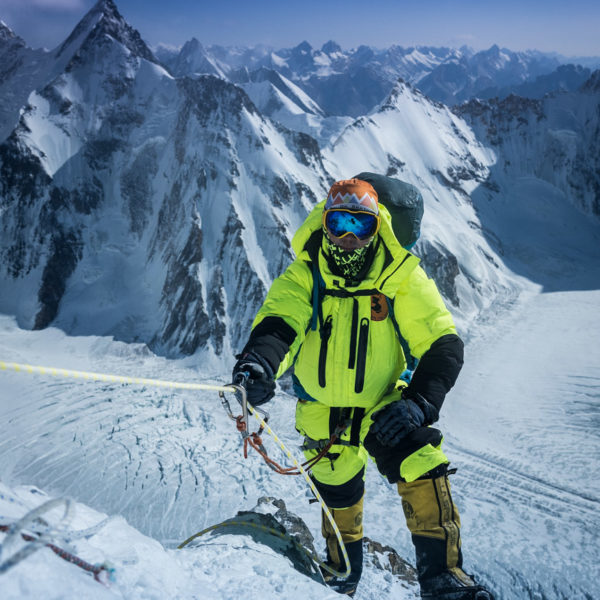 Climber in fluorescent downsuit attached to a safety line standing in front of a mountain